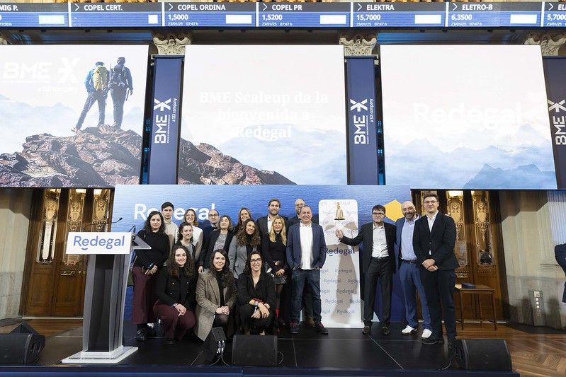 Miembros de Redegal posan bajo el lema BME Scaleup da la Bienvenida a Redegal junto a la campana